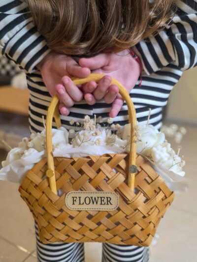 Niña sujetando cesta de mimbre con velas de flores detrás de la espalda para regalo sorpresa