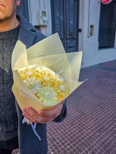 Ramo de velas de soja con margaritas amarillas y blancas sostenido en la calle
