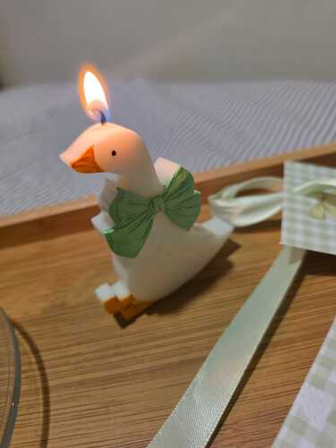 Vela aromática de gansito de soja encendida con moñito verde mint sobre bandeja de madera.