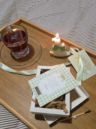 Vela aromática de gansito encendida en bandeja junto a taza de té y caja de souvenir abierta.